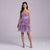 A woman modeling a short, sleeveless purple floral dress with a sweetheart neckline, corset-style bodice, and a tiered tulle skirt, photographed against a plain light gray studio background.