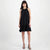 A woman modeling a sleeveless black halter-neck dress with ruffled trim at the neckline and a ruffled hem, paired with black strappy high-heeled sandals against a plain light gray studio background.
