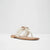 A single flat thong sandal in cream-colored textured fabric with a metallic rose gold chain detail across the strap, set against a plain white studio background.