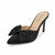 A single black satin pointed-toe mule heel with a large bow on the toe, shown on a clean white background. The insole displays the brand name 'JOURNEE collection'.