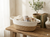 Woven basket on a wooden table with books, plants, and decorative items.