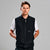 A man wearing a black sleeveless zip-front vest over a white short-sleeve shirt, photographed against a plain light gray studio background. The vest has a small visible SANC logo on the left chest.