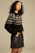 Woman wearing a black and white patterned sweater with a plain background