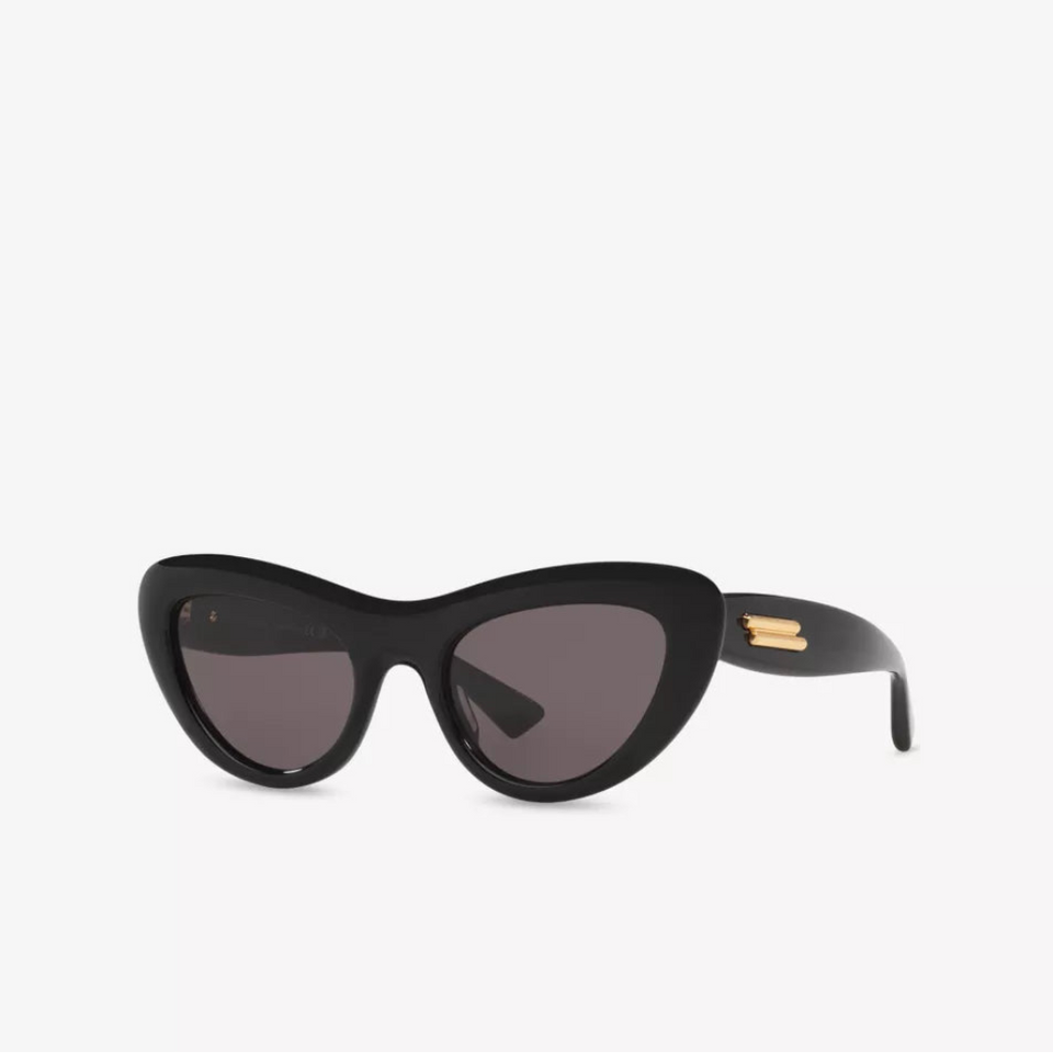 Black cat-eye sunglasses with dark lenses and a small gold-tone logo detail on the temple arm, shown against a plain white background.