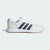 A white Adidas Korkway sneaker with three dark navy stripes, a cream midsole, and a gum brown outsole, shown from a side profile on a light gray background.