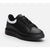 A black leather low-top sneaker with a thick black platform sole, black laces, and a contrasting white side accent, shown on a light gray background.