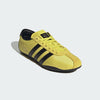 Yellow Adidas sneaker with black stripes on a light gray background