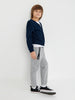 Child wearing a navy sweater, white shirt, gray pants, and black sneakers on a white background