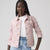 A model wearing a light pink washed denim jacket over a white t-shirt and light blue jeans, photographed against a solid light gray background.