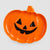 An orange pumpkin-shaped plate with a black carved jack-o'-lantern face, shown on a light gray background.