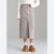 A model wearing a mid-calf, knee-length taupe knit skirt with a front slit, styled with a white fuzzy sweater, white socks, and brown suede slip-on shoes against a neutral gray background.