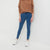 A model wearing blue skinny jeans, a brown sweatshirt, and white sneakers, standing against a plain light gray studio background.