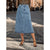 A woman wearing a light blue denim midi skirt with a raw hem, paired with a leopard print top and black strappy heels, standing on a cobblestone street.