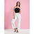 A woman modeling a black halter top with white trim and white wide-leg jeans against a solid pink studio backdrop.