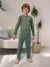 Child wearing green pajamas with a pattern in a room with a couch and plants.