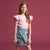 A young girl with long light brown hair stands against a solid dusty rose background, wearing a light pink short-sleeve top with ruffled flutter sleeves and a light blue denim cargo mini skirt.