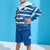 A child wearing a blue and white striped zip-up hoodie with geometric pocket details and matching blue shorts, standing against a bright blue studio background.