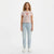 A woman stands against a plain white studio background wearing a light pink lace short-sleeve crop top with a red heart graphic on the chest, light-wash blue jeans, and white sneakers.