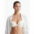 A woman wearing a cream-colored underwire bra, styled with an open white button-down shirt, against a plain white studio background.