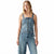 A woman modeling a light blue denim jumpsuit with a square neckline, front zipper, and wide-leg jeans on a plain white background.