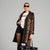 A model wearing a black leopard print trench coat over a white graphic t-shirt, black shorts, and black tights, holding a black leather tote bag against a solid gray studio background.
