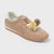 A beige suede sneaker with a white heel tab, brown laces, and decorative yellow and white flowers with brown pom-poms on the side, set against a light gray background.