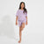 A young girl modeling a light purple short-sleeve pajama set with a matching graphic print, standing barefoot against a plain white studio background.