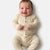 A smiling baby wearing a cream ribbed long-sleeve footless romper with brown buttons, photographed against a clean white background.