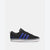 A black Adidas low-top sneaker with three blue stripes on the side, a white rubber sole, and a black laces and tongue, shown against a light gray background.
