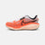 A Nike running shoe in vibrant orange and light pink, featuring a black Swoosh logo, white laces, and a black and white patterned collar, shown against a light gray background.