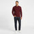A man modeling a ribbed crewneck sweater in burgundy, paired with dark blue jeans and white sneakers, against a plain white studio background.