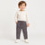 A toddler standing against a light gray studio background, wearing a cream long-sleeve crewneck sweatshirt, dark gray drawstring pants, and white sneakers.