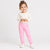 A young child wearing pink patterned sweatpants and a cream long-sleeve top, standing against a plain white studio background.