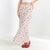 A woman models a high-waisted, floor-length flared skirt with a delicate pink and red floral print on a cream background. She is wearing red strappy flat shoes against a clean white studio background.