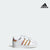 A white Adidas baby girl sneaker with orange and pink stripes and two velcro straps.