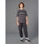A young boy stands against a solid gray studio background wearing a dark gray crewneck t-shirt with a distressed 'BROOKLYN' graphic across the chest, dark gray cargo jogger pants, and black and white sneakers.