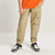 A person wearing beige cargo jogger pants with elastic cuffs, paired with a bright orange t-shirt and black-and-white sneakers, shown from the waist down against a light gray studio background.