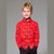 A young boy with blonde hair wearing a red long-sleeve button-down shirt with a small multicolor floral pattern, paired with black pants, standing against a solid gray studio background.