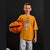 A young boy wearing a yellow-orange t-shirt with a pumpkin skeleton graphic and patterned pajamas, holding a plush jack-o'-lantern against a black background.