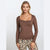 A woman modeling a fitted long-sleeve scoop-neck top in a medium brown color, paired with leopard print pants, against a light gray studio background.