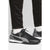 Black Puma turf shoes with white and gray accents, shown on a model wearing black pants and white socks against a light gray background.
