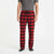 A man wearing red and black buffalo plaid pajama pants with a drawstring waist, paired with a gray t-shirt and dark socks, shown from the waist down on a white studio background.