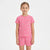 A young girl modeling a pink short-sleeve t-shirt and matching shorts set with a white seashell pattern, set against a plain white studio background.