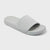 A light gray slide sandal with a wide, single strap and a thick cushioned sole, shown from a three-quarters angle on a light gray background.