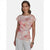 A woman modeling a short-sleeve blouse with a pink and white watercolor floral print, paired with white trousers, against a light gray studio background.