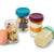 Four clear baby feeding storage jars with colorful screw-top lids, shown on a white background. One jar is open with fruit pieces inside, one has layered fruit and cream, one has layered orange and cream, and one is lying down with pale yellow food inside.