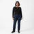 A woman modeling dark blue straight-leg jeans with a black long-sleeve top and black shoes, standing against a plain white studio background.