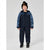 A young boy wearing a dark navy and blue patterned snowsuit with a black beanie and black sneakers, standing against a light gray studio background.