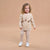 A toddler girl stands against a solid beige studio background wearing a matching beige sweatshirt and jogger pants set. The sweatshirt features a graphic of three brown teddy bears and the text 'Love you, baby love.