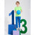 A young boy stands on a small purple block, smiling and holding a blue basketball. He is wearing a bright lime green t-shirt, blue sweatpants, and white sneakers.